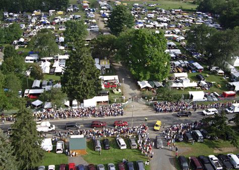 Bird's-eye view of Brimfield Antiques Show with many tents in fields among trees.
