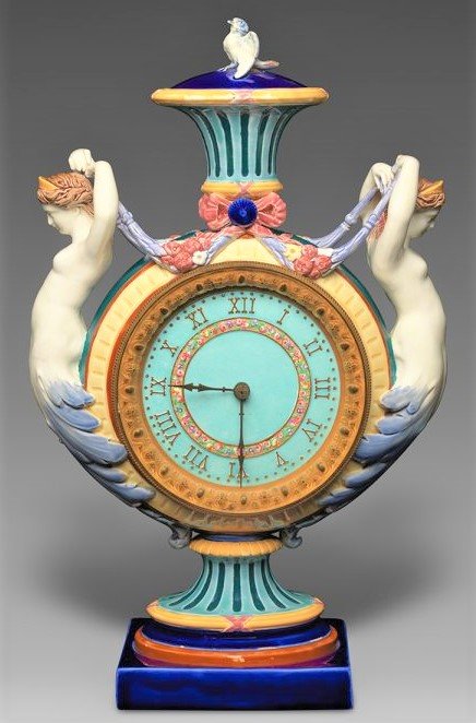 Colorful majolica clock in vase form flanked by mermaid figures, topped with small bird figure.