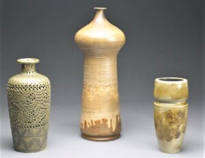 Two vases, one openwork and one solid, and one tall cup, all with neutral finishes.